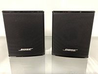 Front view of two black Bose satellite speakers on reflective surface.