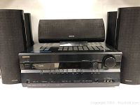 Front view showing AV receiver with display and control knob, flanked by front left and right speakers and center channel speaker on top