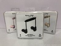 Front view of three boxed Happy Plugs Ear Piece II wireless earphones in pink, black and beige showing packaging and earphone design.