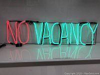 Photo of the illuminated no vacancy LED sign with red neon for 'NO' and blue-green neon for 'VACANCY' mounted on black frame.