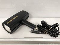 Full view of the handheld Muni Quip K-GP radar gun with attached coiled power cord and cigarette lighter adapter.