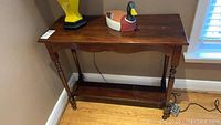 Mahogany console table from the side with a lamp and wooden duck on top, showing wear and scratches.
