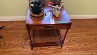 Full view of the wooden side table with a drawer and lower woven cane shelf. Table has items on top including plant pots and decorative pieces.