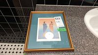 Framed print with two standing abstract figures in soft colors, wood frame with teal mat