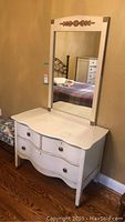 White wooden dresser with curved front drawers and an attached vertical mirror with gold decorative accents.