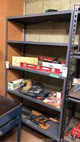 Front view of metal shelving unit showing all 4 shelves with some miscellaneous items on it. Surface wear and basement setting are visible.