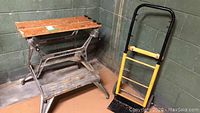 Photo showing the Black and Decker workbench next to the dolly in a corner with concrete walls.