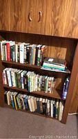 Three shelves of assorted books in wooden shelving unit