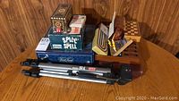 Opted T 15 tripod and stacked board games including Spil & Spell and Trivial Pursuit volume two on wood floor