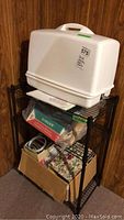 Overall view of sewing machine on wire shelving with notions boxes below