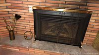 Fireplace tools in brass stand next to brick fireplace with black and brass fireplace screen