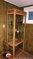 Full view of rope style shelving unit in corner of room with glass shelves and various glassware items displayed.