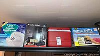 Photo showing all four items on shelf including the boxed Vicks humidifier, Proctor Silex coffee maker, Rubbermaid cooler, and Shiatsu Master Elite massager.