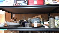Photo of multiple cookware and kitchen items arranged on a shelf, highlighting pans, graters, and glassware.