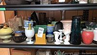 Shelf with assorted crystal, glass, ceramic vases, bowls, metal pitcher and plant pots showing condition and variety