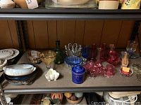 Shelf showing cranberry glassware, pottery pieces, decanter, and decorative items