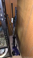 Three right handed golf clubs leaning against wood panel wall with purple golf bag base