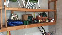 Wide view of shelf with blue tarps, green pots, terra cotta pots, garden hose attachments, and various garden and camping items