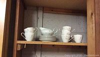 White porcelain cups, creamers and saucers arranged on a wooden shelf