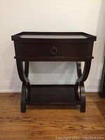 Front view of handcrafted dark wood end table with drawer and curved legs on hardwood flooring.