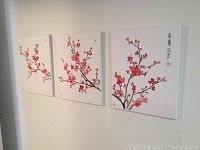 Three canvas panels hung on a wall showing a continuous cherry blossom branch across them.
