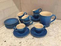 All included items: eight blue demitasse cups and saucers, plus one larger mug. Cups and saucers are stacked and arranged on a kitchen counter.