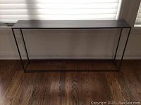 Front view of metal hall table against window with blinds, showing the rectangular frame and top surface.