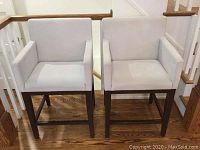 Front view of two light beige upholstered bar stools on dark wood frames