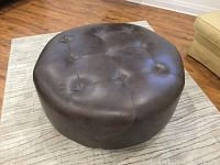 Front-right angle of the round dark brown leather ottoman showing tufted top