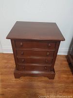 Front view of cherry wood night table with four drawers and round wooden knobs on hardwood floor.