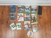 Photo of assorted Xbox 360 game cases and gaming accessories on wooden floor under white wall.