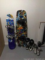 Photo of Burton snowboard, Ronix wakeboard, and boots standing against wall.