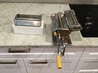 Marcato Atlas 150 pasta maker with yellow handle crank and pasta cutter attachment on countertop.