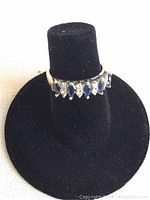 Front view of ring on black display showing alternating marquise sapphires and round diamonds.