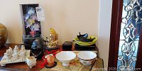 Overview of Asian themed items including plates, cups, vase, fish figurine, lamp, and various small decor items on a table near a doorway.