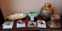 All items in the lot shown together on a table for scale and overview including decorative plates, vases, urn, and bowls.