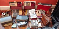 Overview of multiple vintage Polaroid cameras with original cases and accessories arranged on a red surface