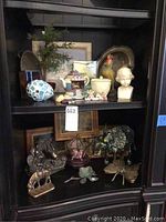 Shelf with assorted decorative pieces including bust, mosaic egg, stained glass, figurines and metal plates.