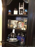 Full view of a dark wood display cabinet shelf holding snow globes, figurines, trays, and crystal pieces.