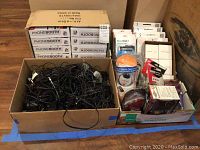 Wide shot of the lot showing several boxes of Phonebooth phone mounts, a box filled with assorted AC adapters and cables, and a box of various other small electronic accessories including Kindle Fire folios and chargers.