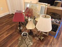 Four table lamps with different lampshades arranged on wooden floor, showing various styles and one new shade with tag.