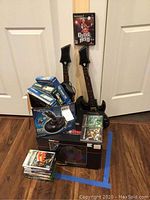 Photo showing all items in the lot including two Hero Power guitar controllers, game discs, Logitech WingMan controller box, GameStop PS3 steering wheel box.