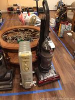 Hoover WindTunnel vacuum YG120 and Pelonis oil heater placed side by side on wood floor with other items in background