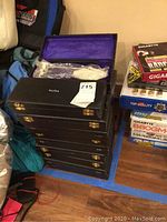 Stack of 18 black carrying/storage cases labeled Sterling, each with brass clasps and purple velvet interiors.