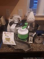 Full lot of kitchen appliances and tools on countertop including mixer, rice cooker, spiral slicer, cake pan, and food scales
