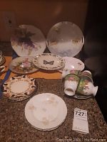 Overall view of decorative plates and cups arranged on table including various floral designs, scalloped edges, and ornate borders