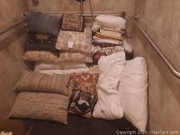 View of assorted pillows and folded blankets stacked and arranged on floor against wall with grab bars.