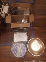 Boxes with metal catering pans and trays along with large metal bowl and some graters