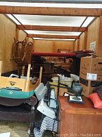 Interior of storage container showing wooden desk/cabinet, stacked wicker lounge chairs, boxes and other items