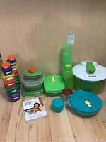 Photo showing the assortment of food storage containers including small rectangular containers with orange lids, various round containers with green and blue lids, and the AR&Cook salad spinner with white base and green handle; also includes 21 Day Fix Eating Plan book on surface.